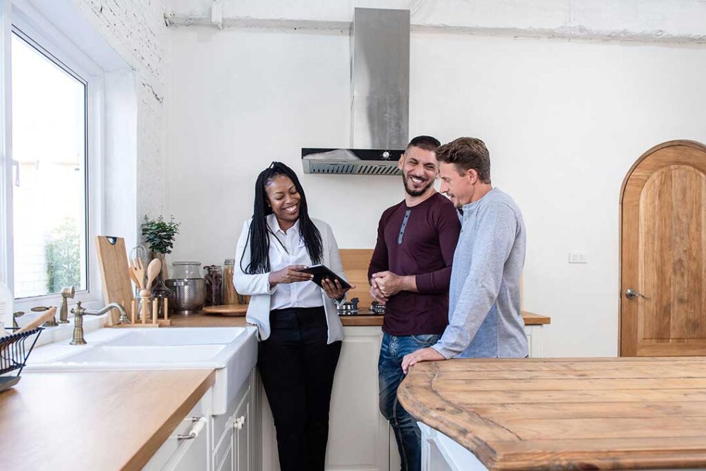 A couple and a real estate agent reviewing paperwork and costs at a closing table with documents and keys visible.
