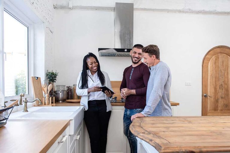 A couple and a real estate agent reviewing paperwork and costs at a closing table with documents and keys visible.